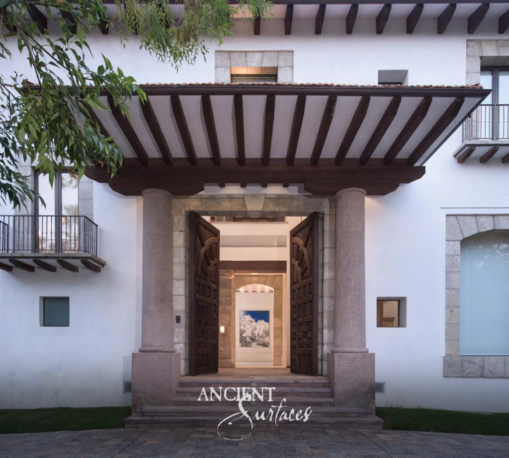 Villa entrance framed by twin reclaimed limestone columns and limestone block surrounds, with carved timber doors above worn antique stone threshold steps