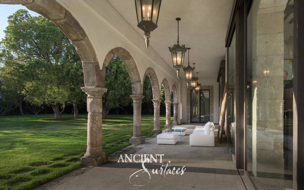 Arcaded loggia of weathered antique limestone columns and arches opening from reclaimed limestone paving onto the lawn of a Mediterranean villa