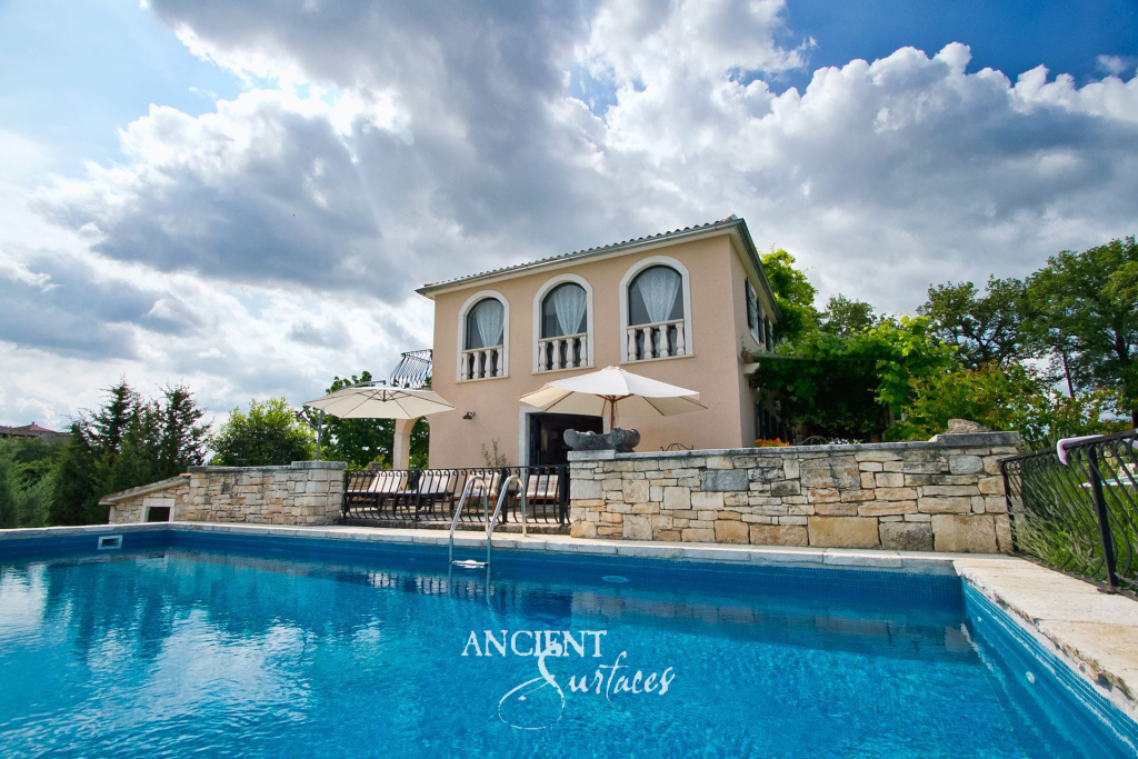 Swimming pool edged in antique limestone coping finished by hand, below a retaining wall of coursed salvaged limestone blocks and a hillside villa