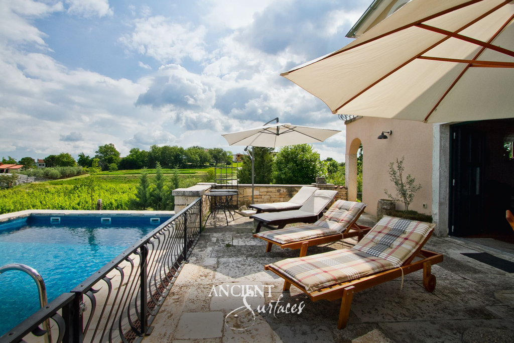 Weathered antique limestone terrace paving laid around poolside loungers, meeting a low garden wall of salvaged limestone blocks
