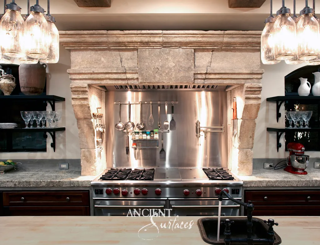 Reclaimed limestone kitchen hood carved from aged blocks and set on stone corbels above the range, between runs of chiseled limestone countertop