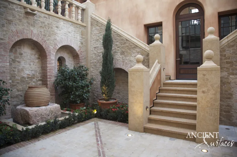 Courtyard stair in golden limestone with turned balusters and ball topped piers, rising past brick arches to a stone framed door