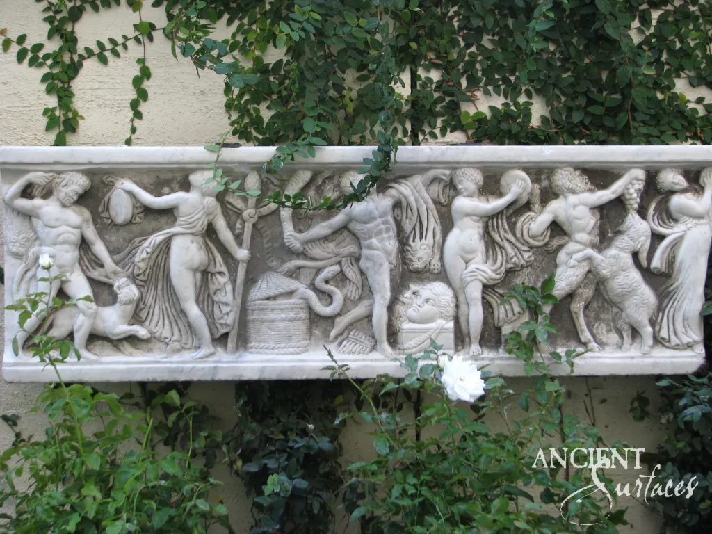Carved marble frieze of a Roman Bacchic procession with nymphs and satyrs, mounted on a garden wall among ivy and white roses