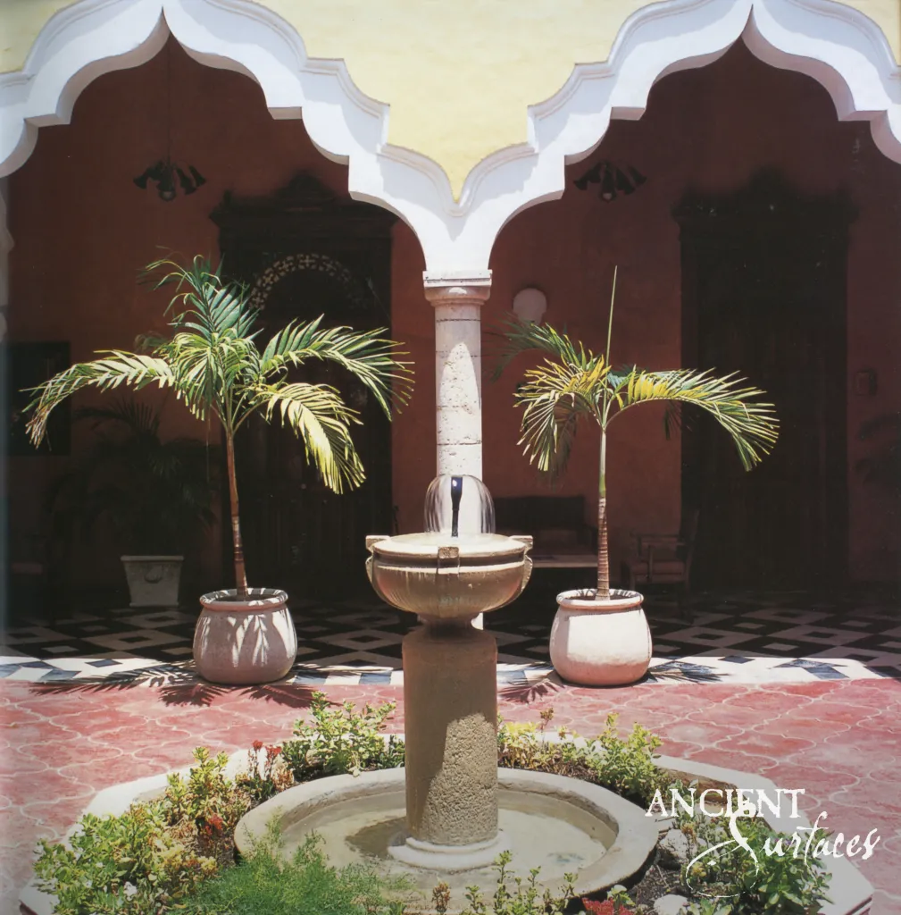 Cylindrical limestone fountain lifting a carved bowl on a stone pedestal in a scalloped arch loggia between potted palms