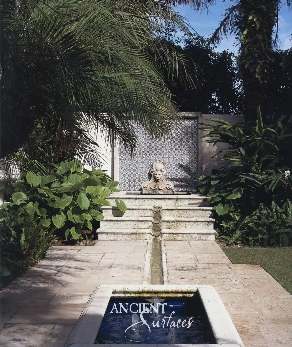 Limestone wall fountain with a sculpted lion mask spout feeding a tiered channel and a rectangular basin set flush into antique limestone paving